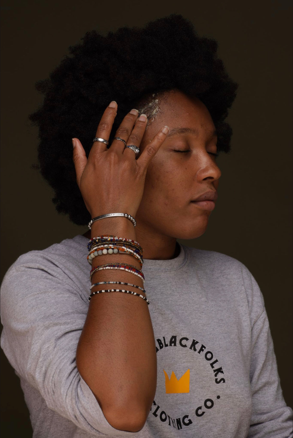 A person with their eyes closed, applying "Erinma" Hair food to their textured hair. 