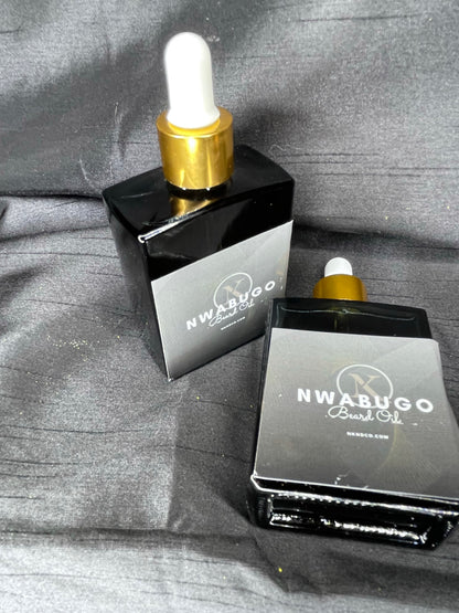 Two bottles of Nwabugo Beard Oil with droppers, one standing upright and the other lying down, on a textured grey surface.