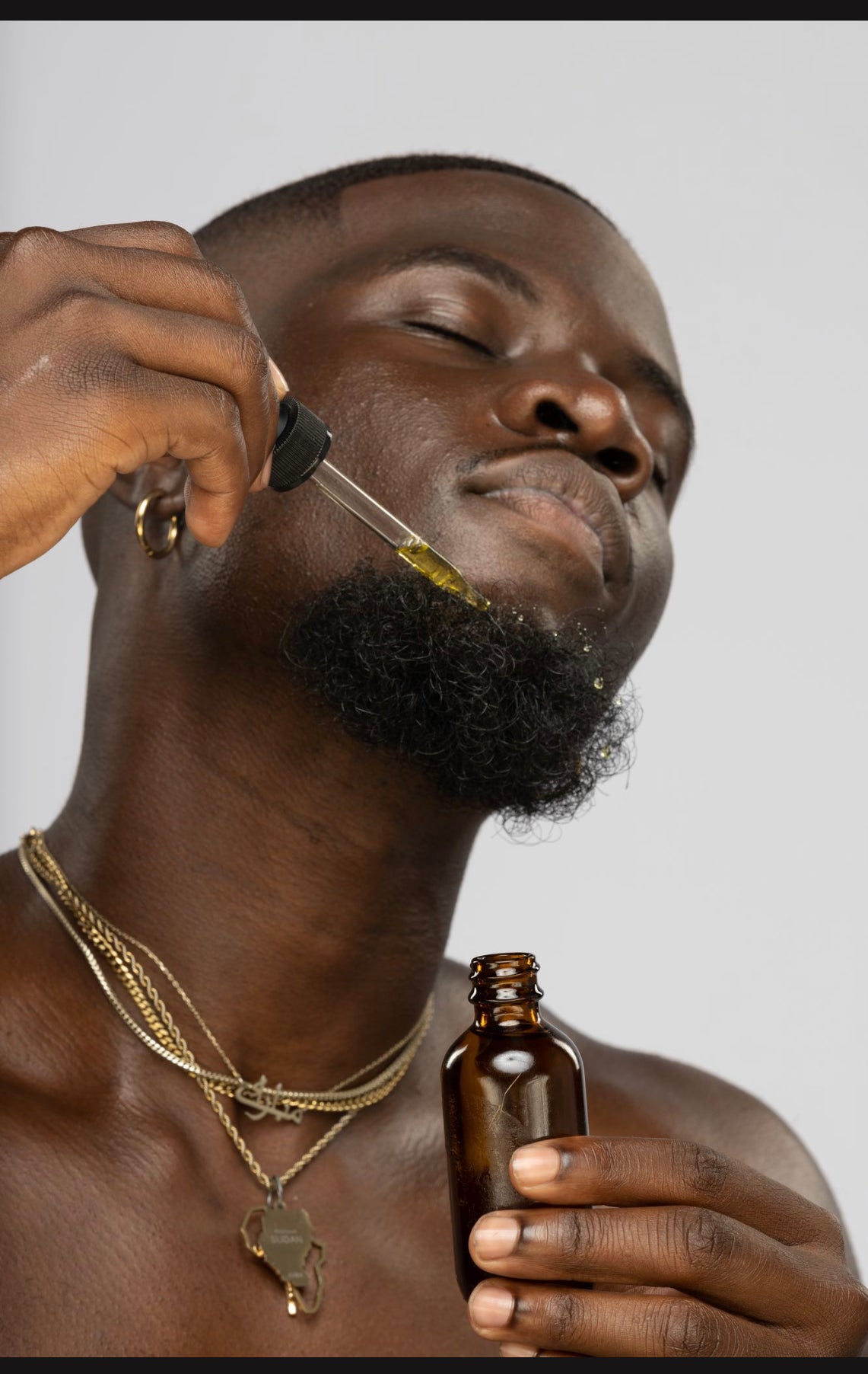close up image of a man applying "Nwabugo" Beard OIl to his beard with  dropper