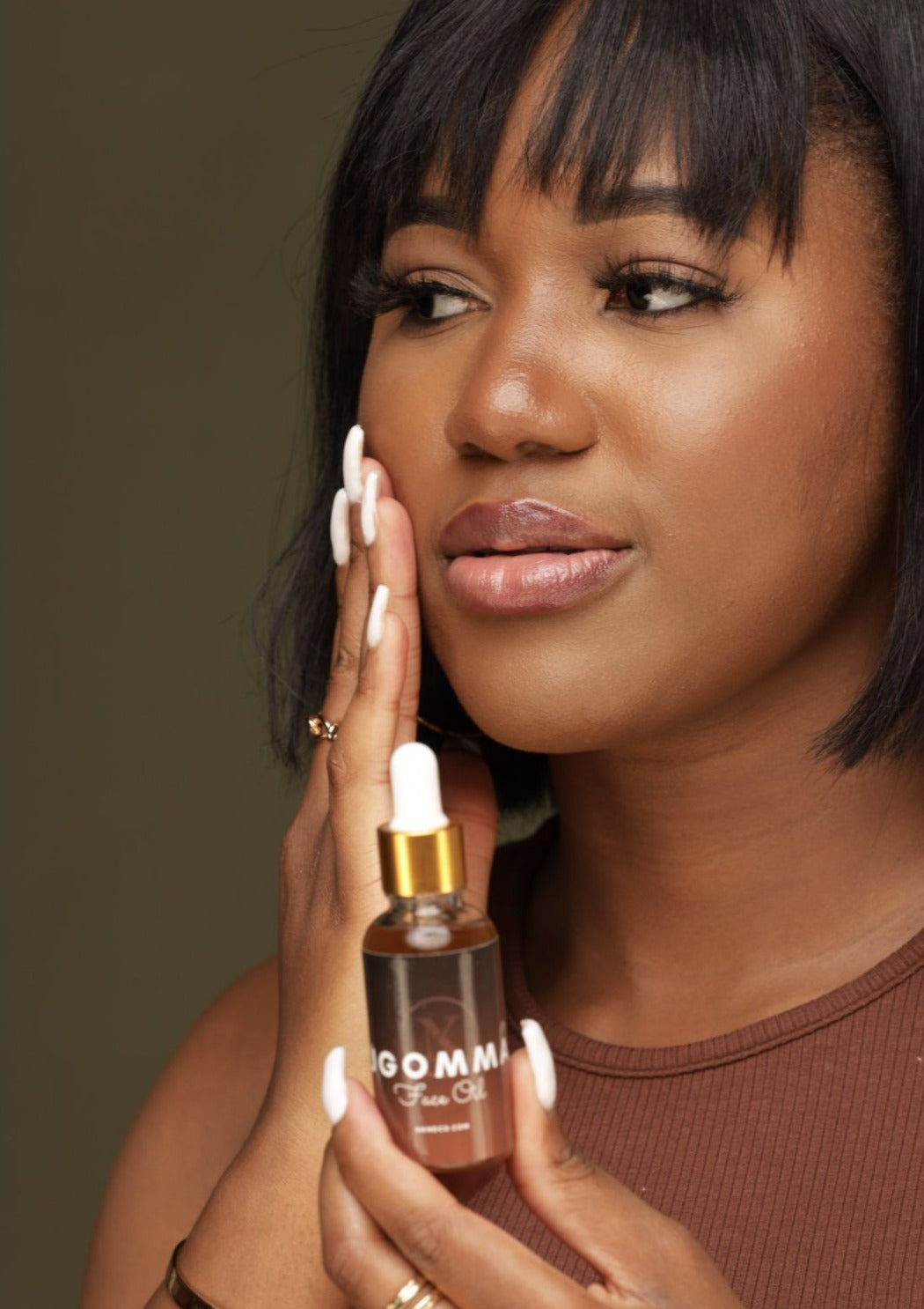 A person holding a bottle of Ugomma Facial Oil while rubbing the oil to their face.