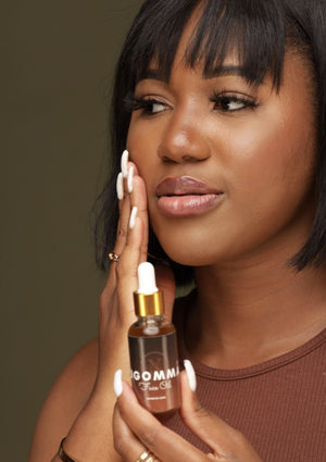 A person holding a bottle of Ugomma Facial Oil while rubbing the oil to their face.